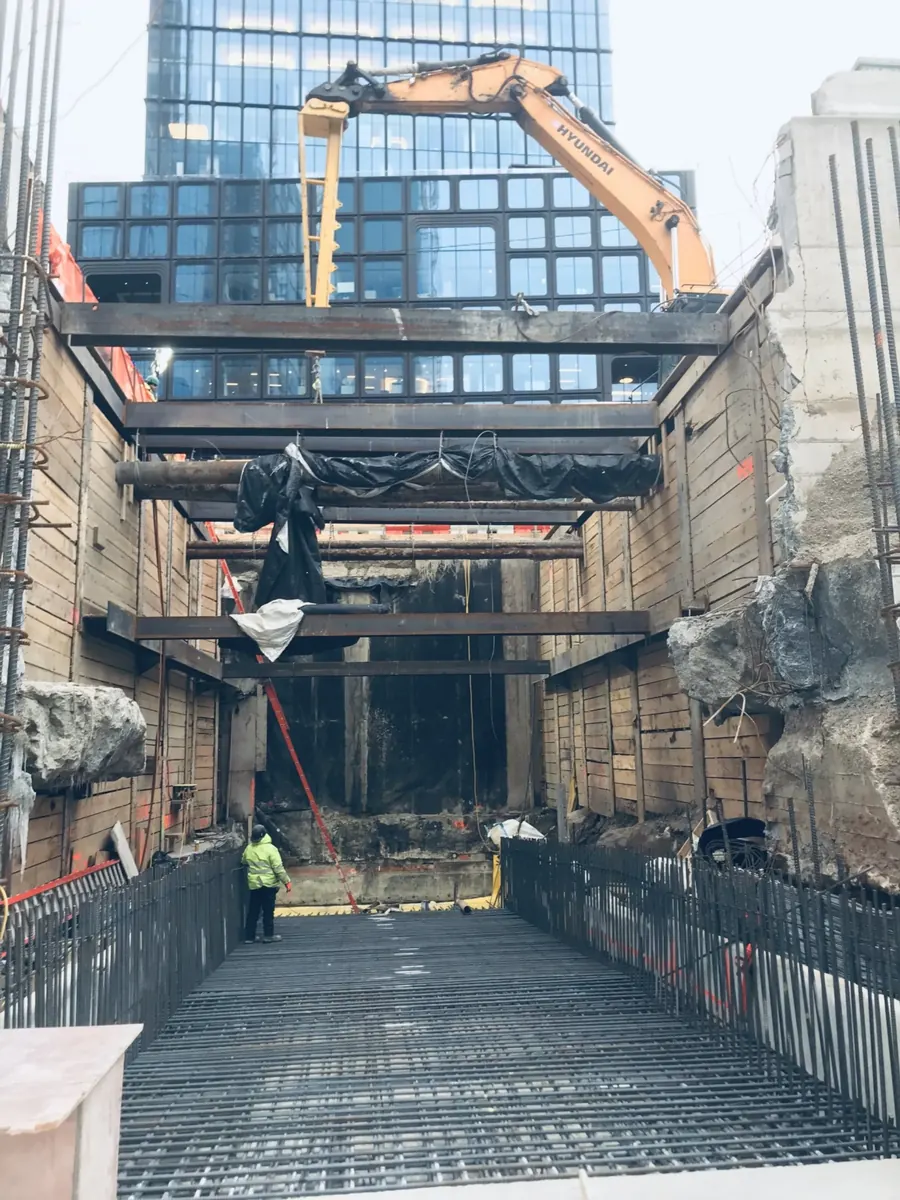 Deep shored excavation with a reinforcing mat beside a glass tower